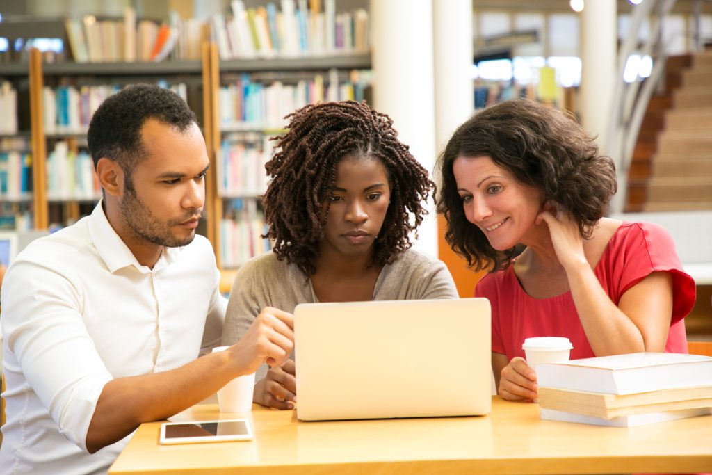 Three people in front of a laptop in a library.