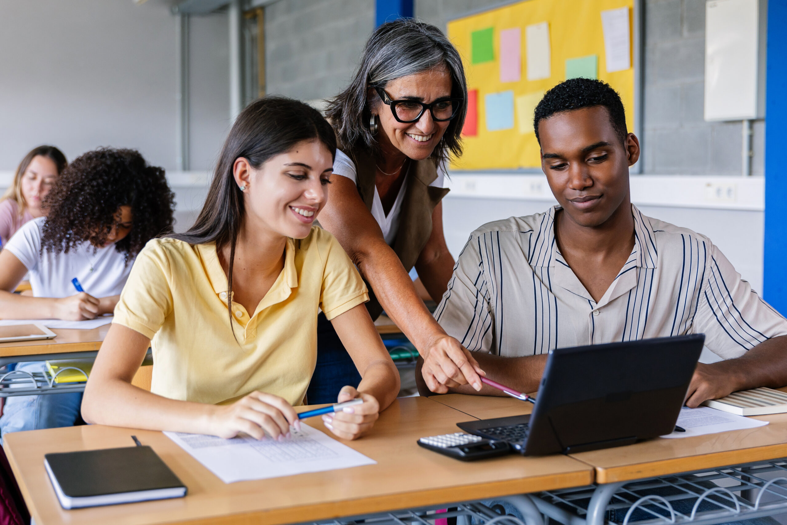 High school educator working with two students on a laptop